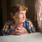 Elderly, sad-looking woman gazing out the window by the kitchen table